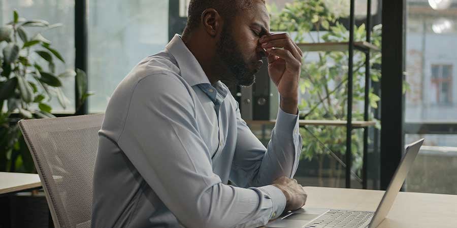 Man sitting at his computer while pinching the bridge of his nose because he's stressed