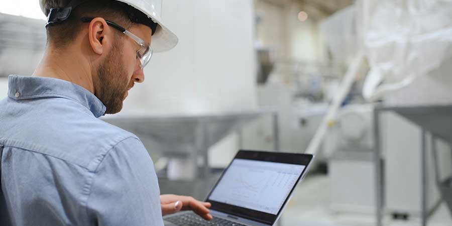 Man wearing a hard hat and saftey goggles in heavy machinery area looking at computer