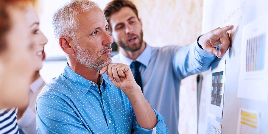 Thoughtful manager reviewing presentation at whiteboard with three team members 