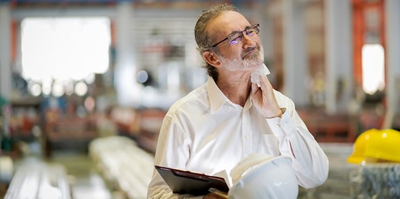 Business man standing on production floor stressed wiping his neck with a towel