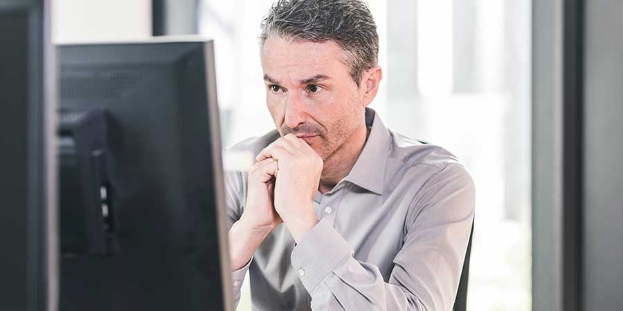 Worried man looking at computer screen in a gray button down shirt. 